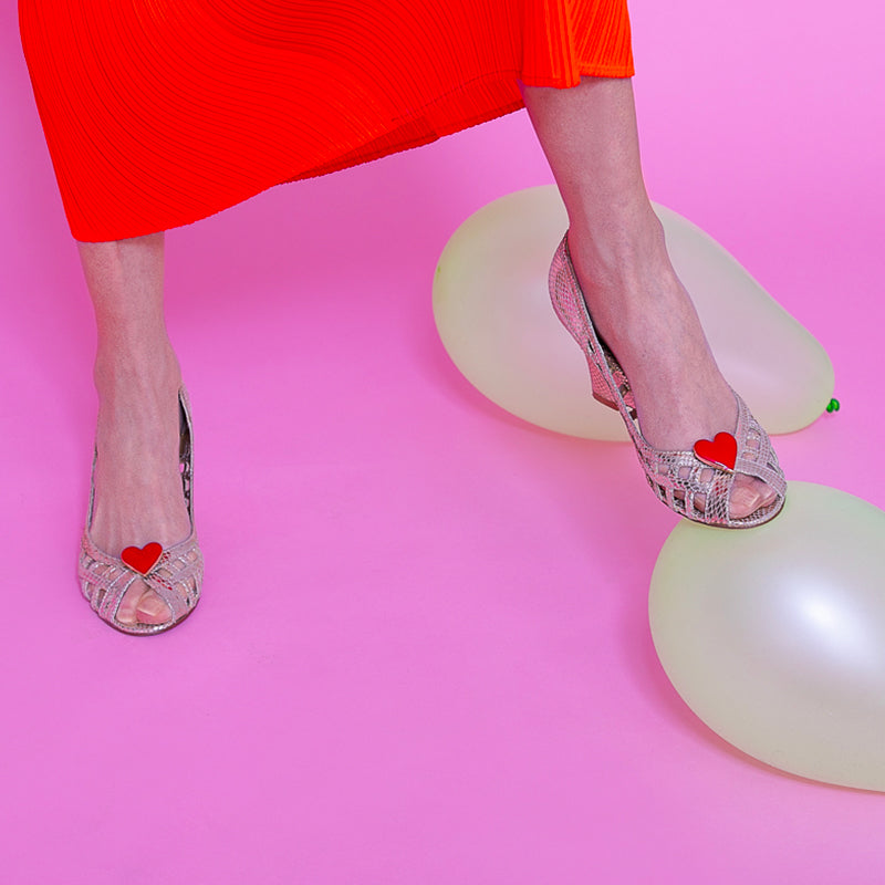 Bijou clip en forme de cœur rouge porté sur sandales tressées argentées
