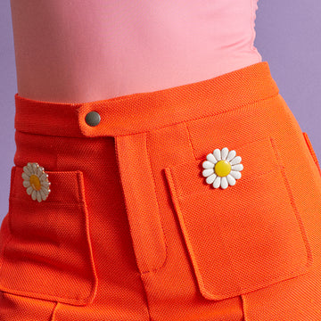 Bijou clip en forme de marguerite porté sur poche pantalon orange