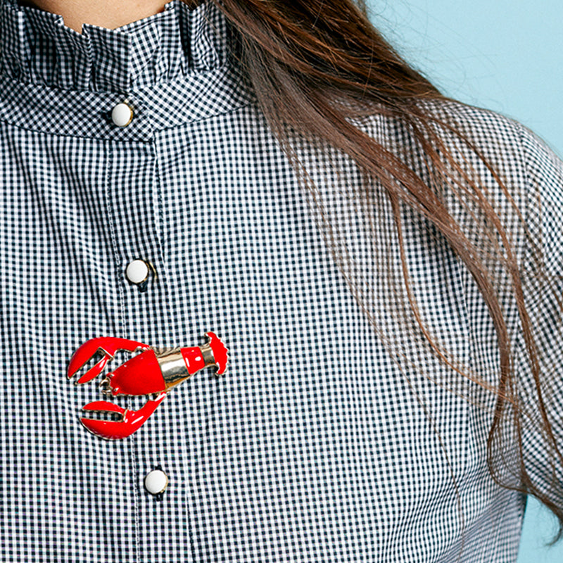 Bijou clip en forme de homard rouge porté sur boutonnière chemisier à carreaux
