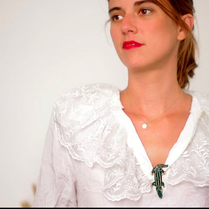 Bijou clip en forme de crocodile vert porté sur décolleté chemise blanche