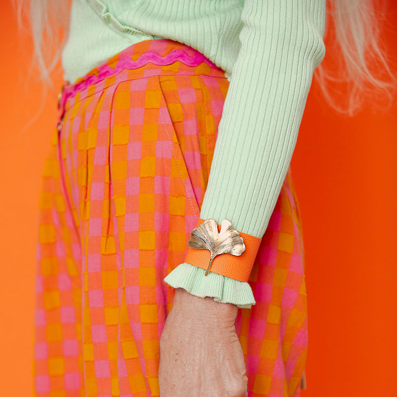 Bijou clip en forme de feuille de gingko dorée sur manchette cuir orange pull vert clair pantalon à carreaux