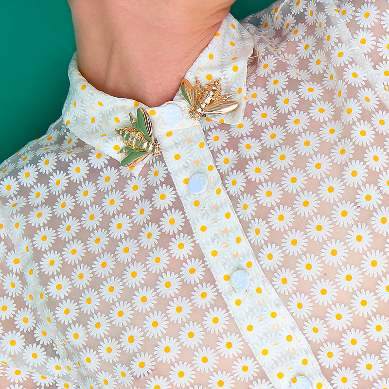 Bijou clip en forme d'abeille dorée porté sur col de chemisier à marguerites