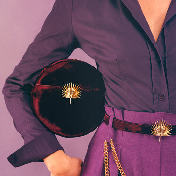 Bijou clip en forme de palmier doré porté sur sac en velours et ceinture pantalon violet