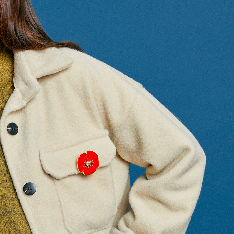 Bijou clip en forme de coquelicot rouge porté sur veste moumoute beige