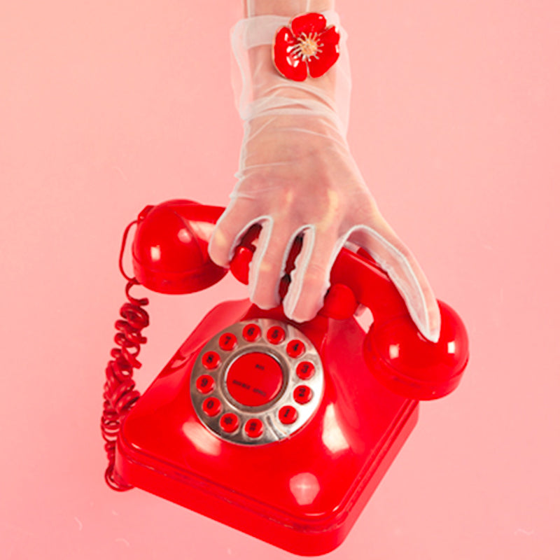 Bijou clip en forme de coquelicot rouge porté sur gant et téléphone rouge