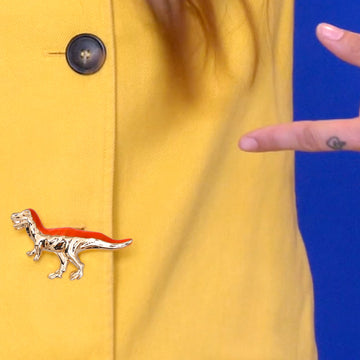 Bijou clip en forme de dinosaure T-rex doré et orange sur boutonnière veste jaune