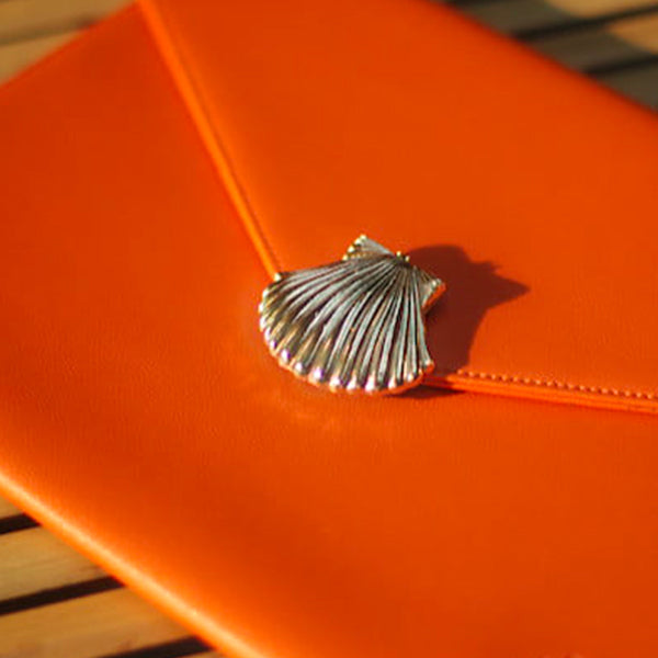 Bijou à clipper en forme de coquillage doré porté sur pochette orange